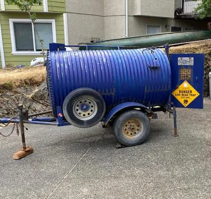 A blue barrel-shaped bear trap on a trailer