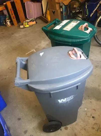Two residential waste bins, one grey and one green, inside a garage