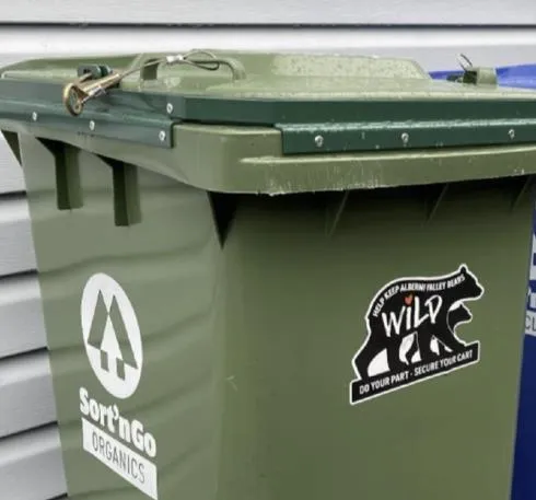 A large brown metal community garbage bin enclosure with a "Household Garbage Here" sign
