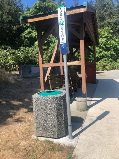 An open-topped concrete garbage can at a bus stop