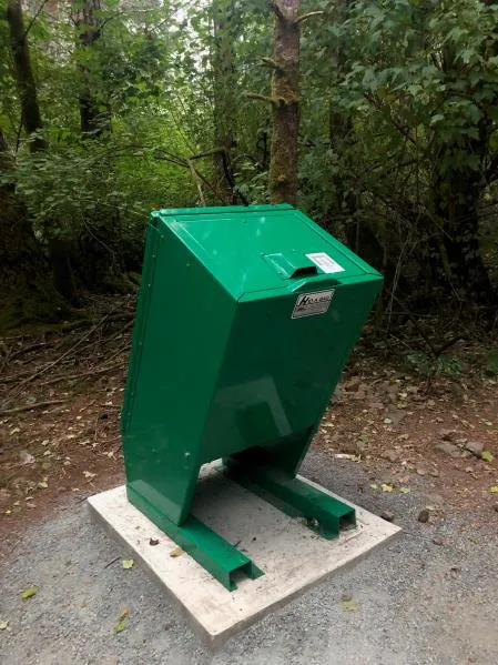 An open-topped concrete garbage can in a park setting