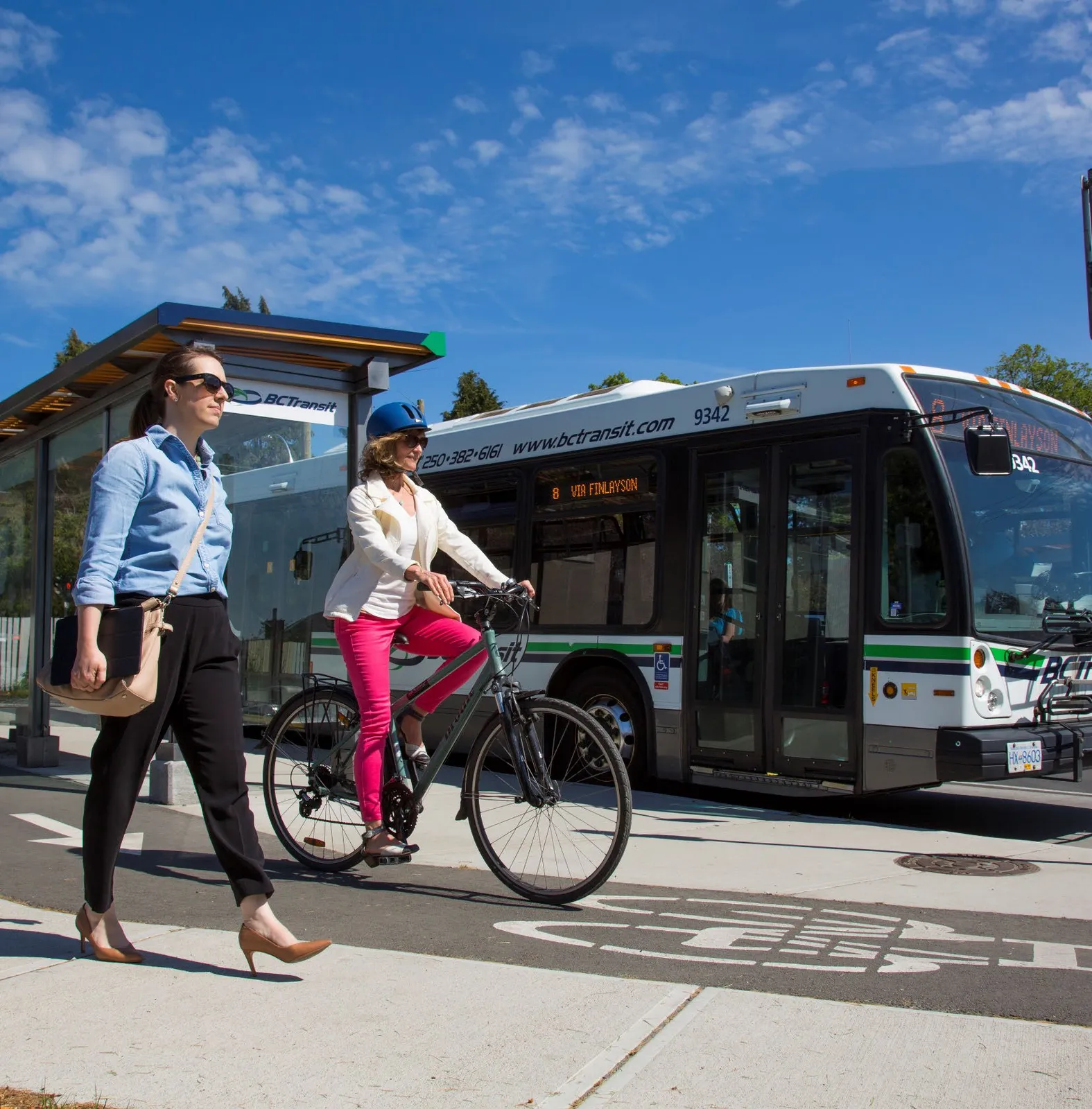 People walking and biking at a bus stop with a BC Transit bus