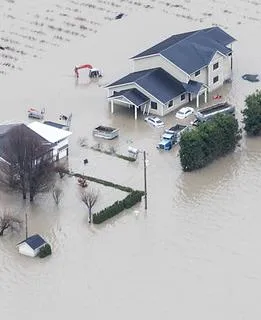 Aerial view of a large residential house and several vehicles completely surrounded by floodwaters in Abbotsford