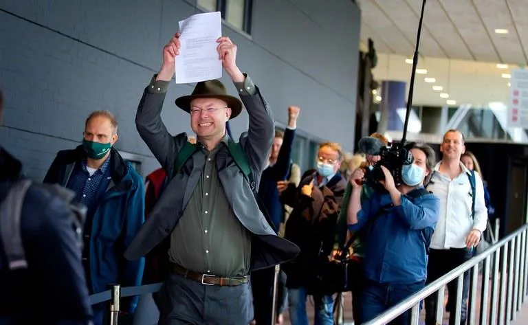 A man in a hat holding up a legal document in a celebratory gesture, leading a group of people.