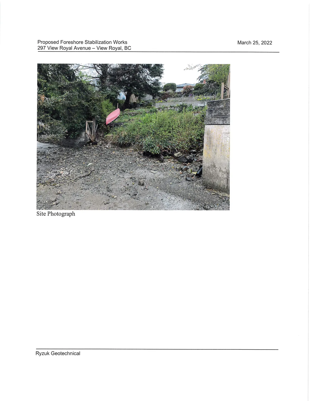 Site Photograph showing the existing vegetated slope, a red canoe, and a concrete seawall on an adjacent property at the shoreline of Limekiln Cove.