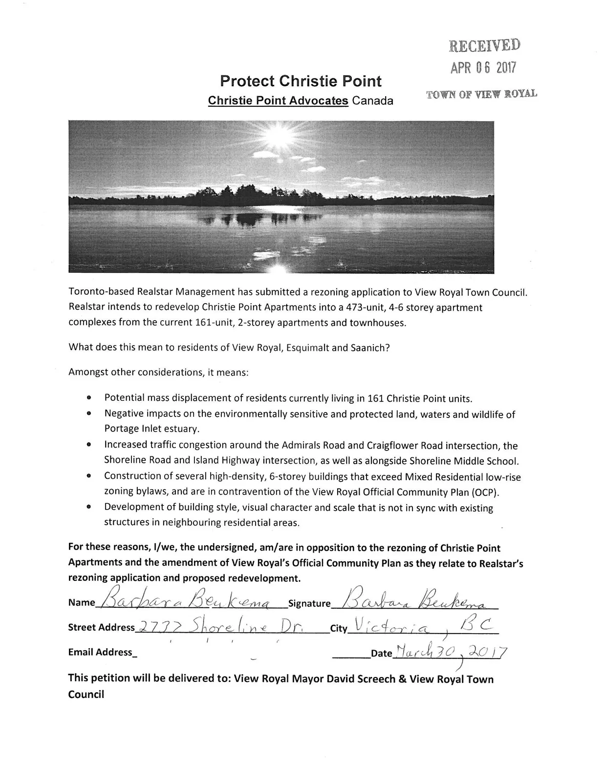 Black and white photograph of a sun setting over a body of water with a tree-lined shore