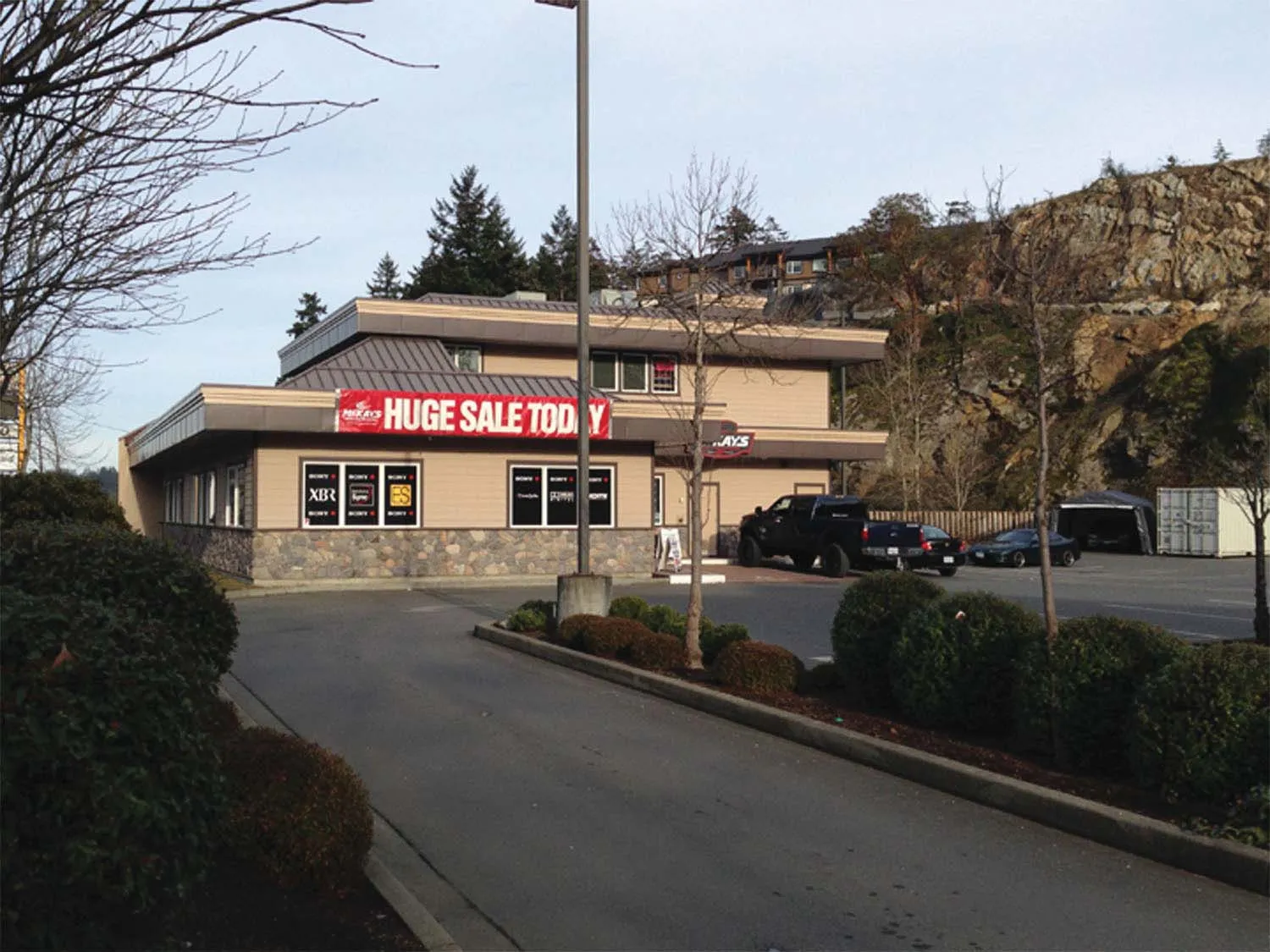Distant view of the existing building from the road, showing a large red banner that reads "HUGE SALE TODAY".