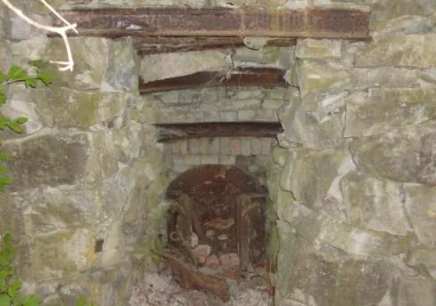 Stone-lined opening of a historic structure, possibly a lime kiln, with moss and surrounding vegetation