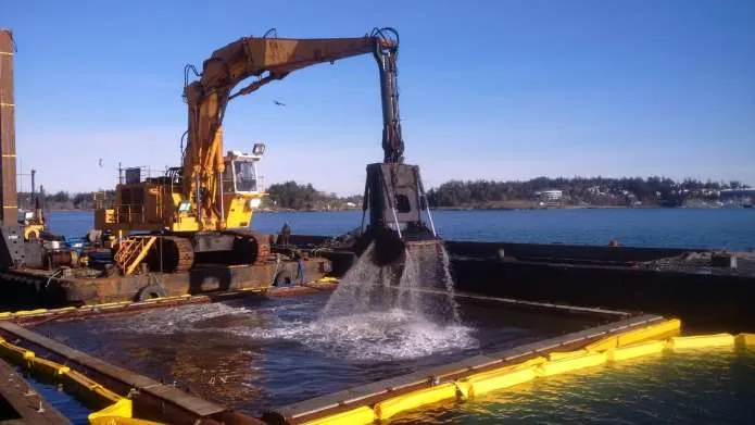 Heavy excavator dredging material from a barge