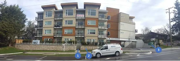Photograph of the completed building with callouts 1, 2, and 3 indicating changes to the walkway, planters, and transformer location