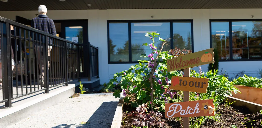 A decorative wooden sign in a resident garden at Sarah Ross House that reads "Welcome to our Patch"