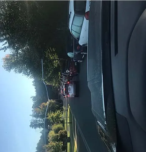 Photo taken from inside a vehicle looking out at a long line of cars backed up on a residential street during the morning.