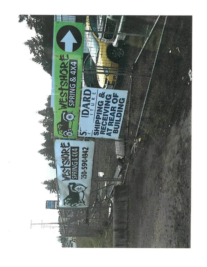 Multiple signs attached to a chain-link fence, including banners for "WESTSHORE SPRING & 4X4" and a sign for "STANDARD FURNITURE SHIPPING & RECEIVING AT REAR OF BUILDING".