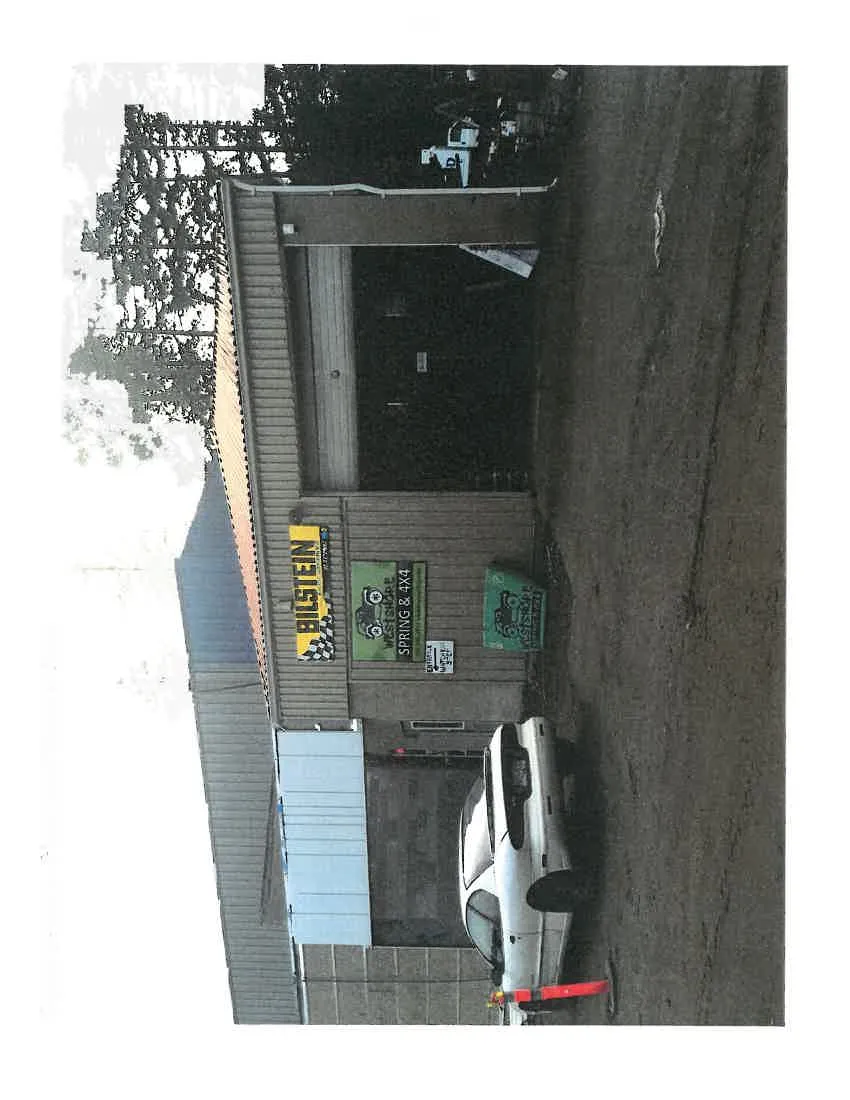 Exterior of a commercial building featuring a "BILSTEIN" sign and "WESTSHORE SPRING & 4X4" banner signs, with a white car parked in the foreground.