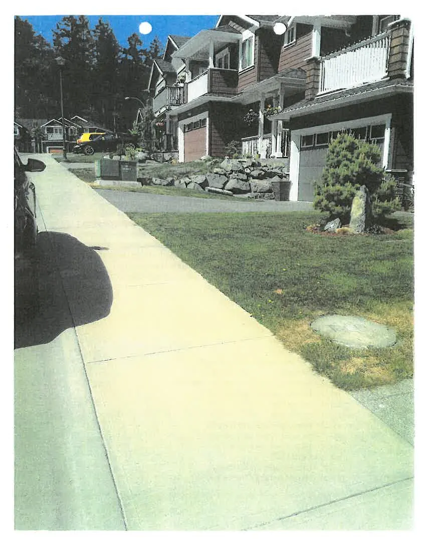 Photograph of a sidewalk and street fronting a row of houses, showing the driveway approach and property boundary