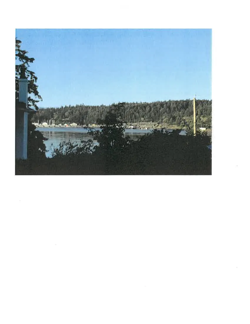 Photo showing a scenic view of a harbour with trees and a house chimney in the foreground
